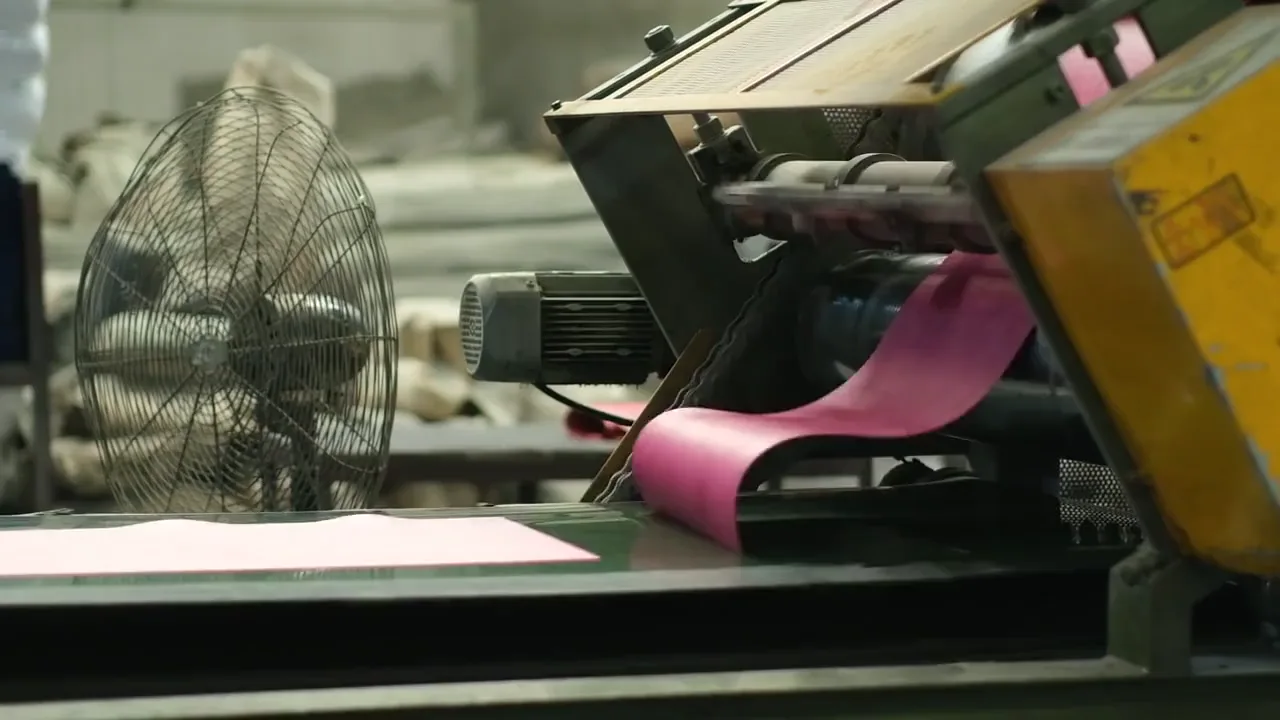 Close crop of pink paper moving through representative printing machinery